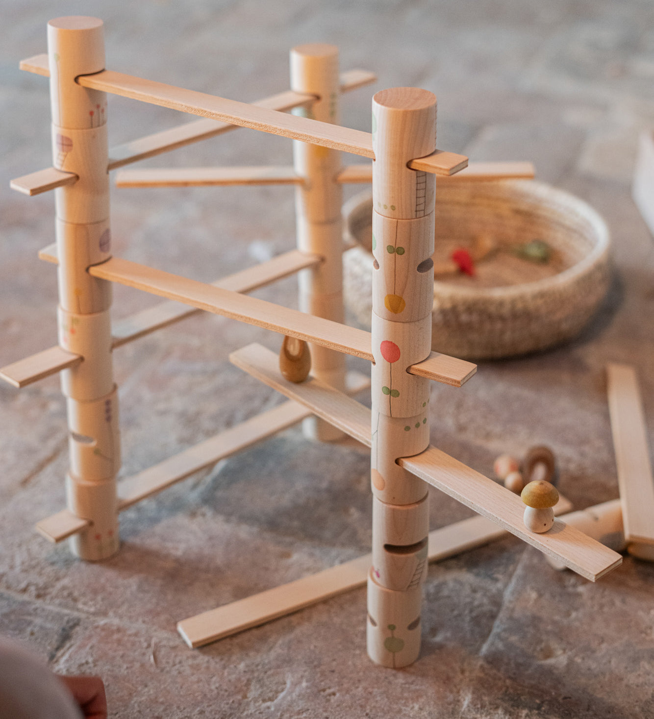 Grapat wooden woodland set on a stone floor- Showing a combination of handcrafted and painted wooden tubes and planks with painted flowers, ladders and window detailing. 