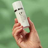 A person holding the Green People Age Defy+ Daily SPF30 Moisturiser - 30ml in their hand on a green background