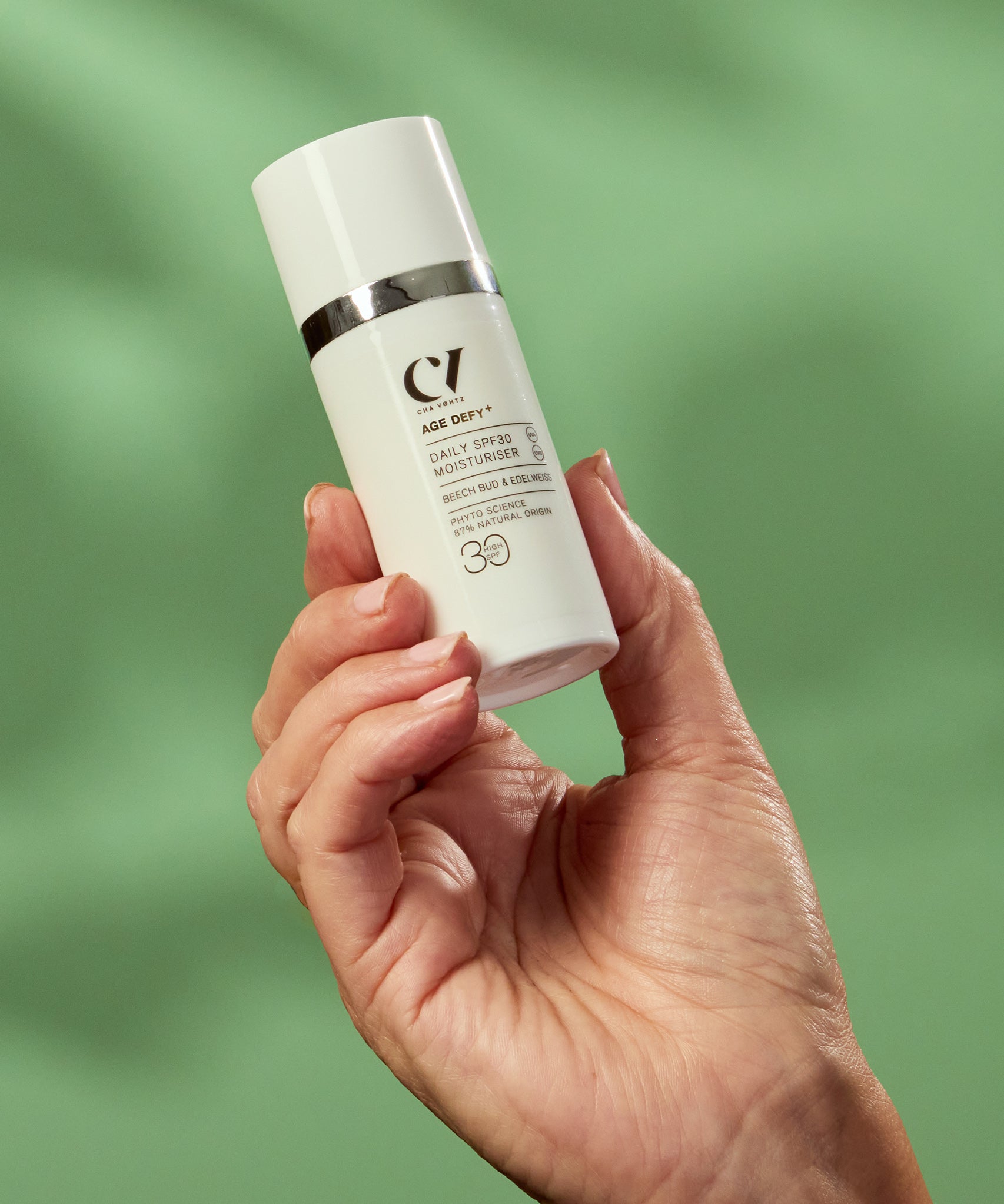 A person holding the Green People Age Defy+ Daily SPF30 Moisturiser - 30ml in their hand on a green background