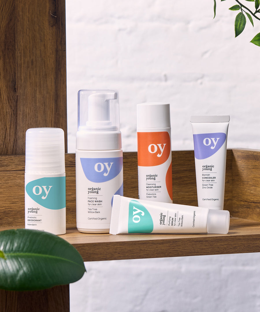 The full collection of the OY! Organic Young skincare range which includes deodorant, face wash, moisturiser, concealer and serum. All the items are stood on a wooden shelf, with a white backgorund