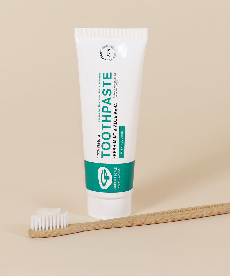 The Green People Natural, Fresh Mint & Aloe Vera Toothpaste with Fluoride on a beige background with a bamboo toothbrush in front of the toothpaste tube