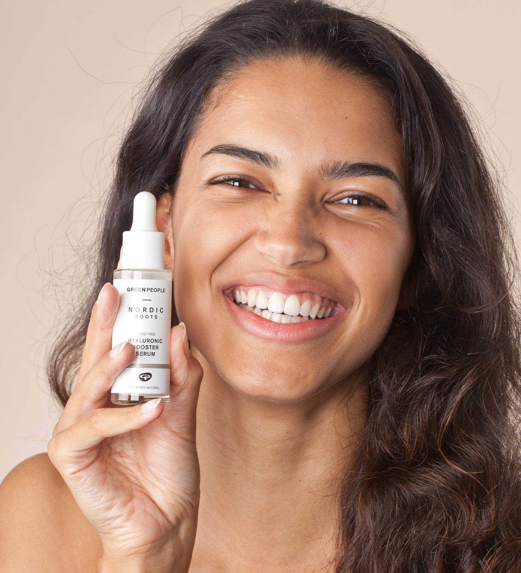 A person with a big smile on their face, holding the Green People Nordic Roots Hyaluronic Booster Serum in their hand