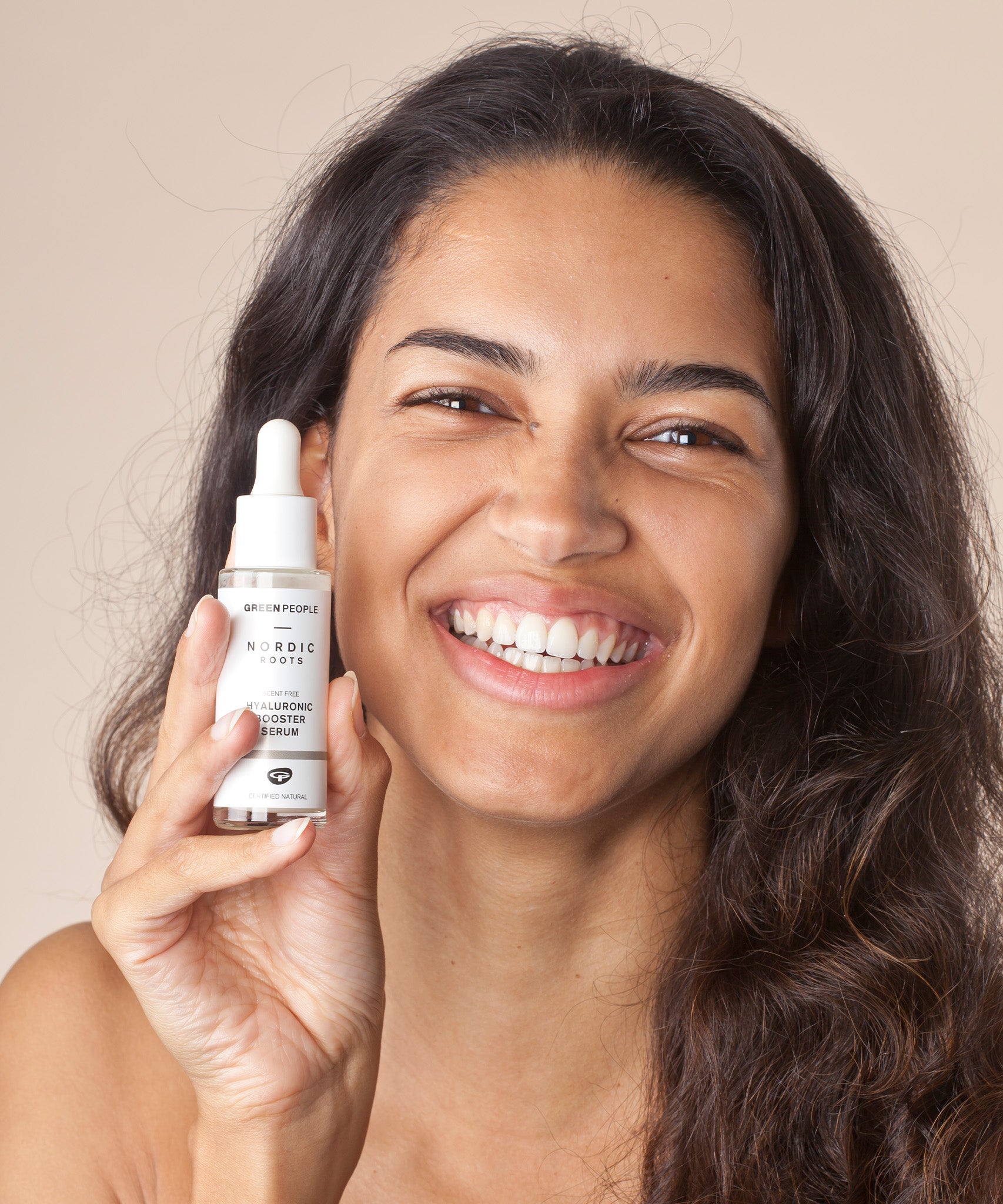 A person with a big smile on their face, holding the Green People Nordic Roots Hyaluronic Booster Serum in their hand