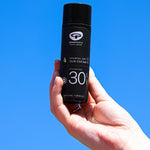 A person holding the Green People Sports SPF30 Mineral Facial Sun Cream 50ml in their hand, with a blue sky in the background