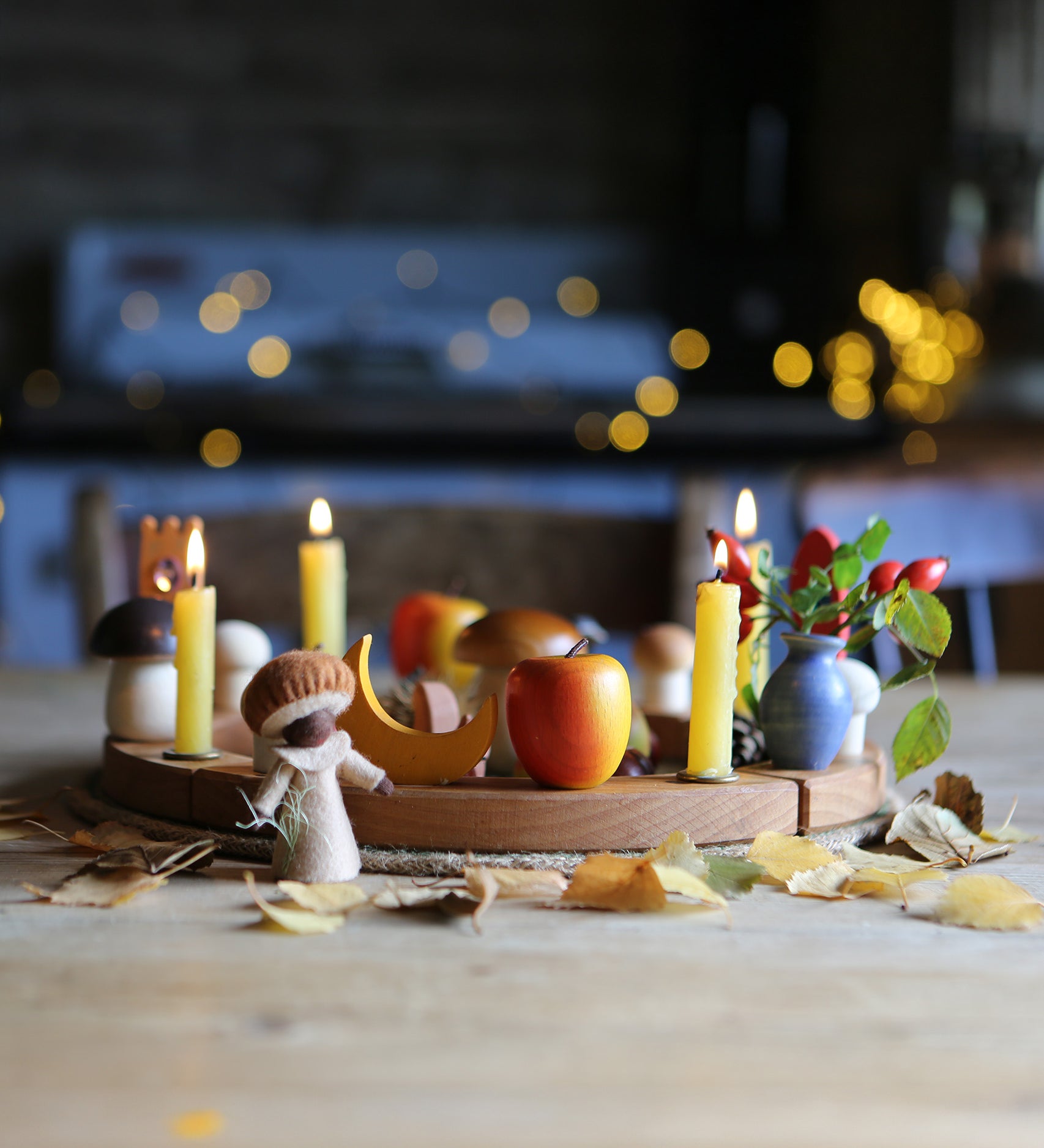 A beautiful Autumnal display made using a Grimm's Wooden Celebration Ring. little leaves are scattered in front of the ring, with colourful decoration and candles in the little holes.