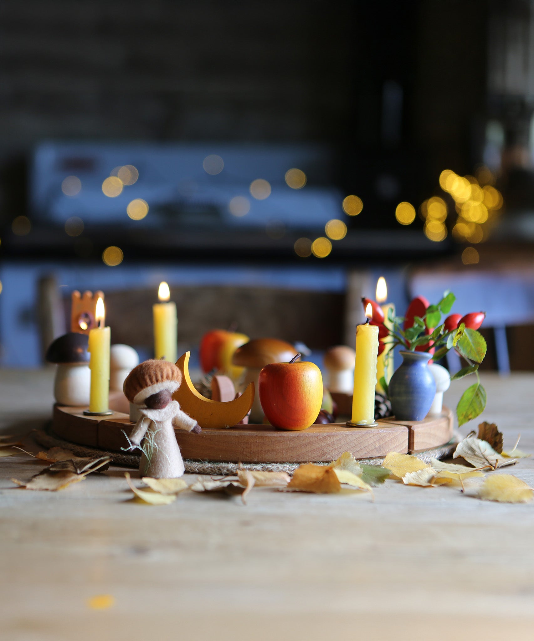 A beautiful Autumnal display made using a Grimm's Wooden Celebration Ring. little leaves are scattered in front of the ring, with colourful decoration and candles in the little holes.