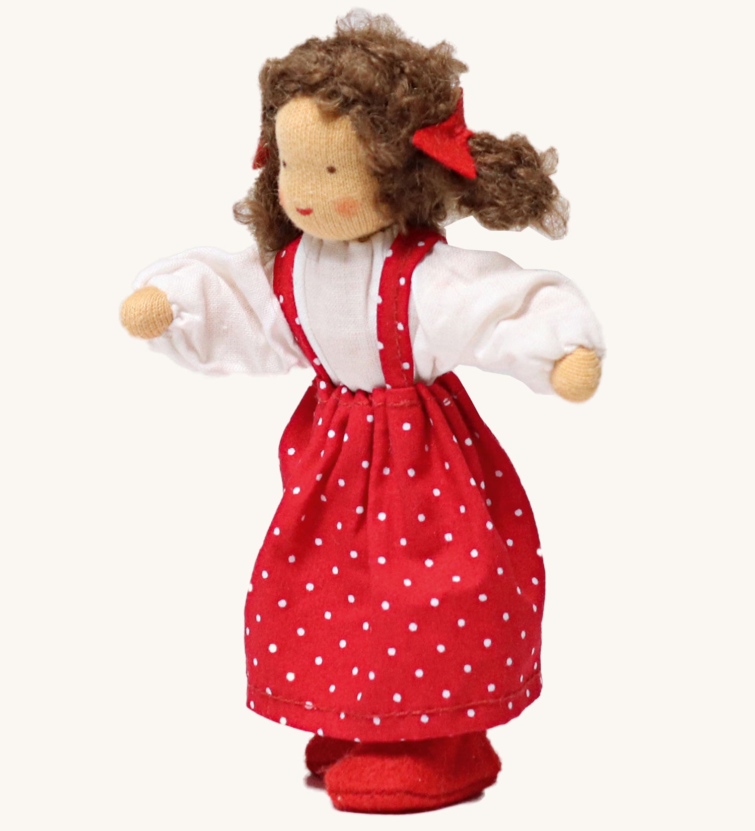 Grimm's Brown Haired Girl Doll - Lana, has brown hair and is wearing a white top under a red dress with white spots all over and is Waldorf inspired. The image is on a cream background