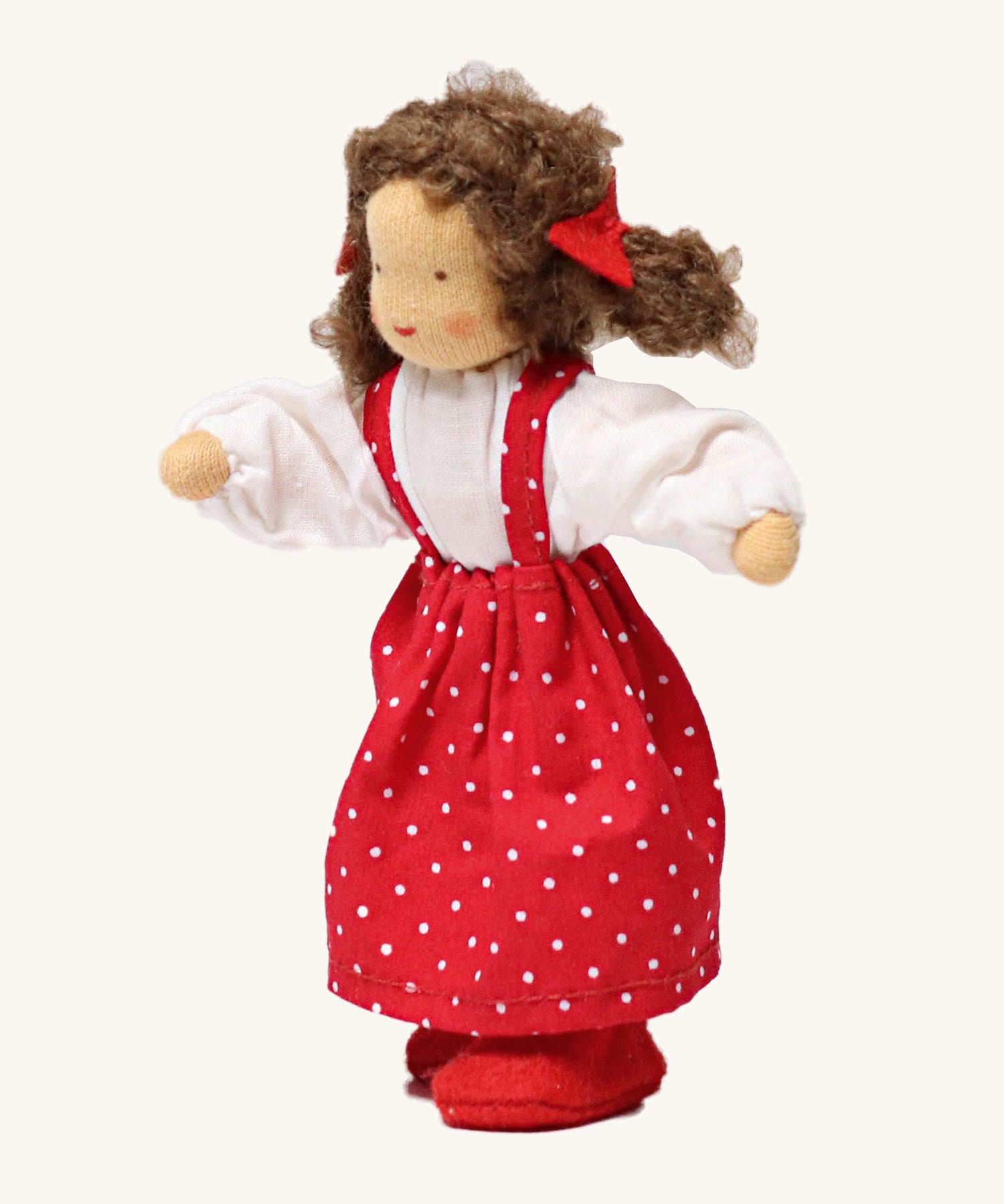 Grimm's Brown Haired Girl Doll - Lana, has brown hair and is wearing a white top under a red dress with white spots all over and is Waldorf inspired. The image is on a cream background