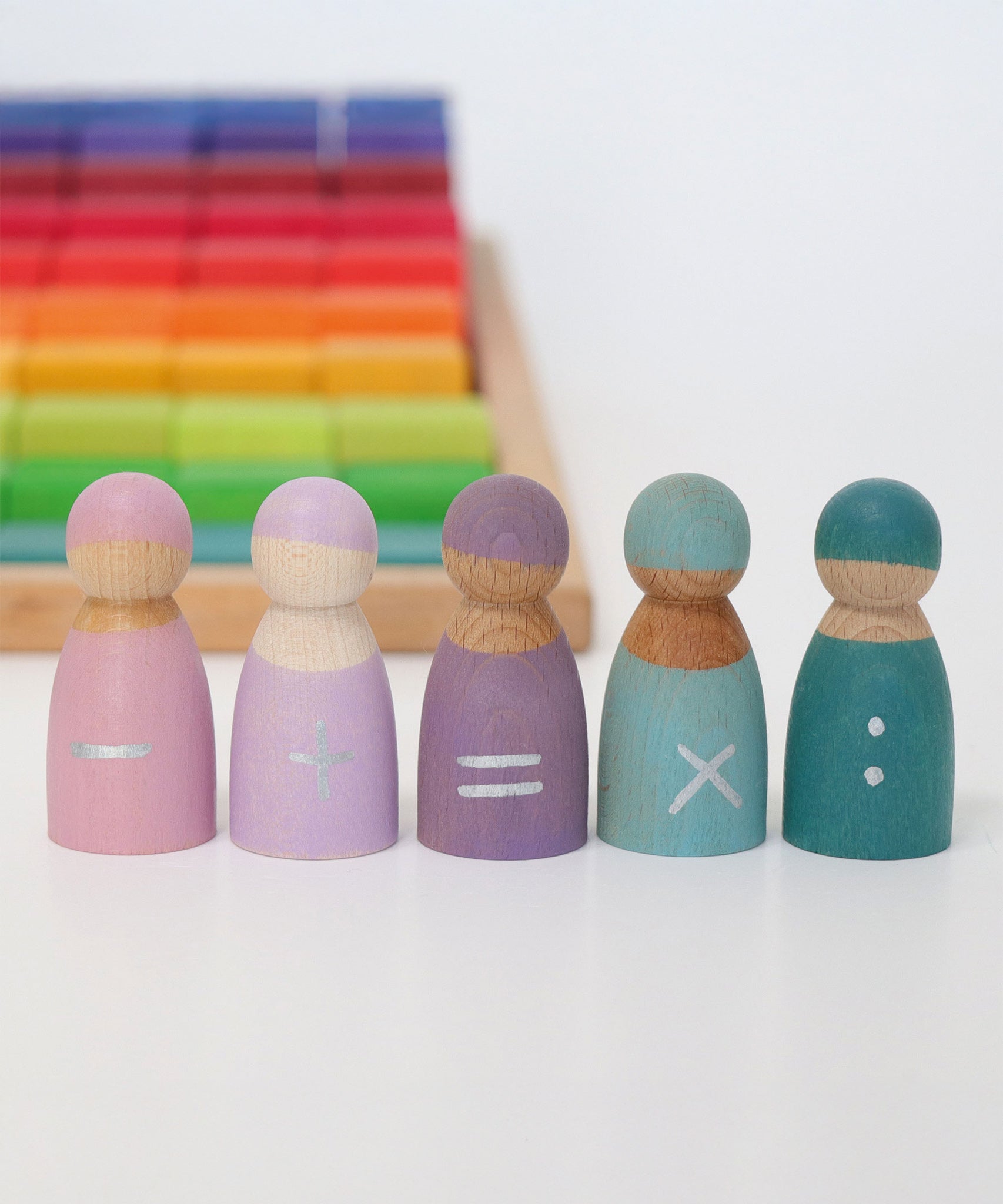 The Grimm's 5 Maths Friends peg dolls all stood in a row with a rainbow Grimm's toy in the background