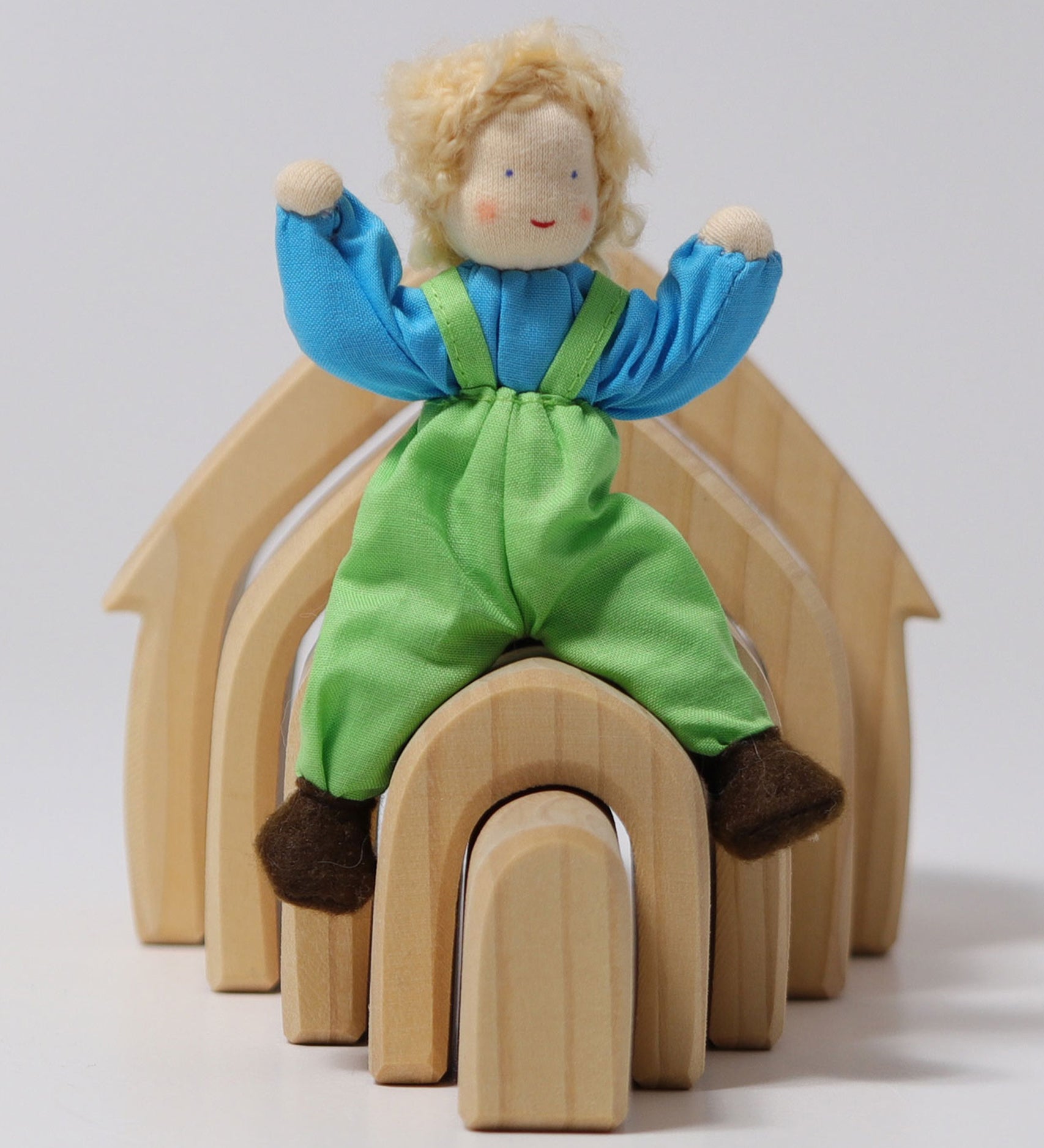 Grimm's Blond Boy Doll - Linde is sat on top of a Grimm's Natural Wooden house with its arms bent up, to show the flexibility of the arms and legs