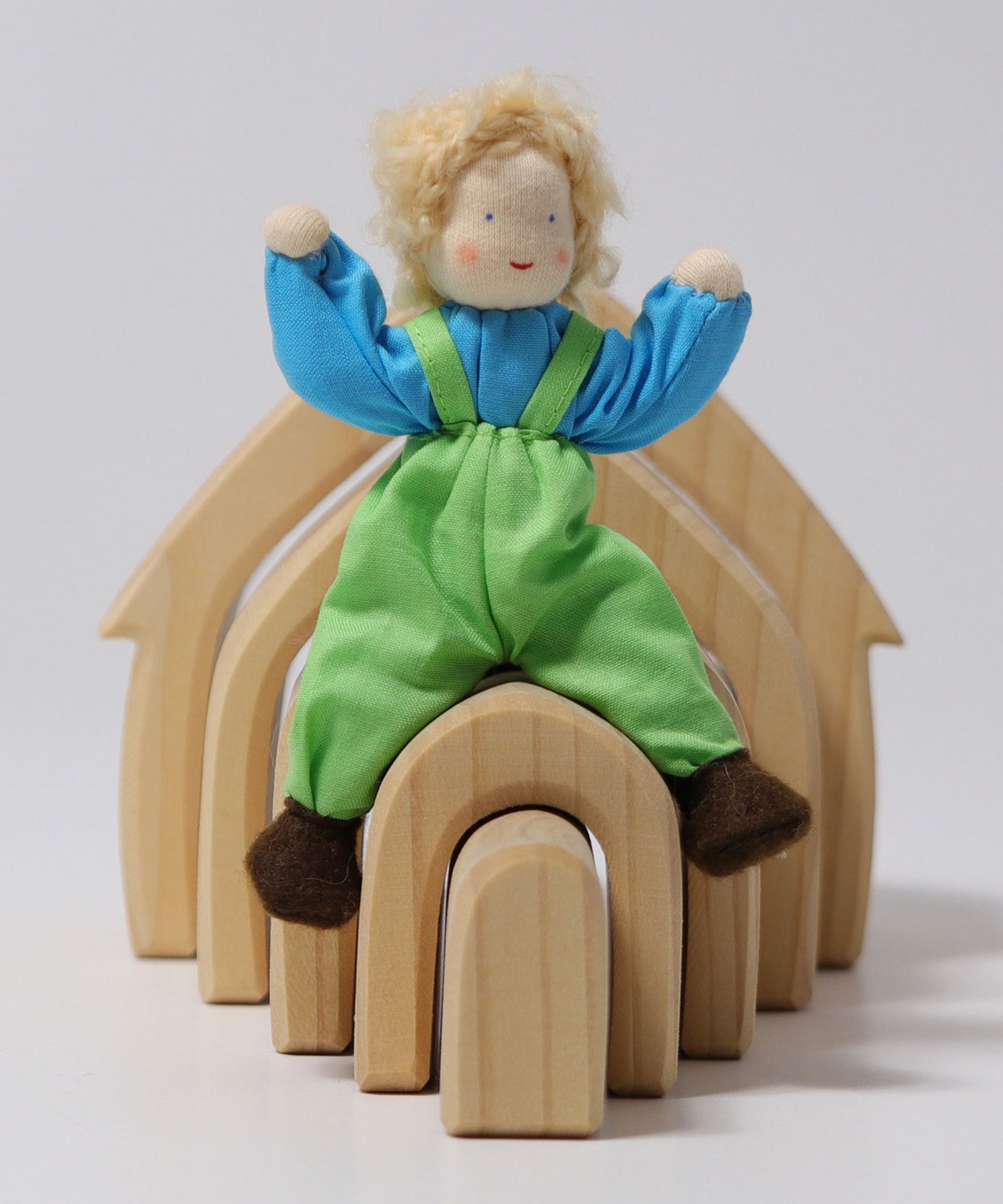 Grimm's Blond Boy Doll - Linde is sat on top of a Grimm's Natural Wooden house with its arms bent up, to show the flexibility of the arms and legs