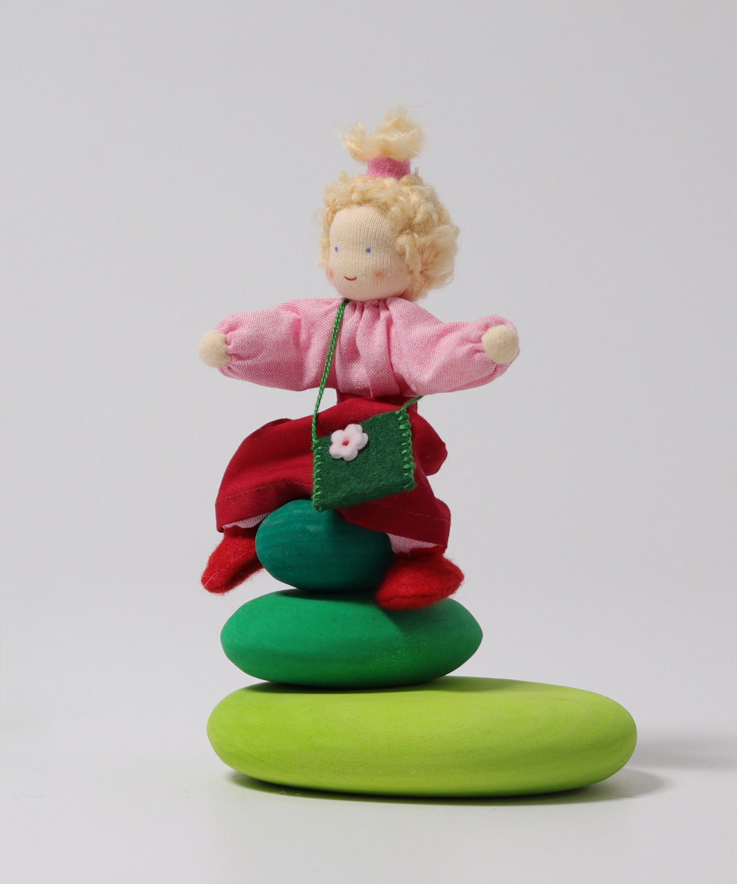 Grimm's Blonde Girl Waldorf Doll sat on top of the Green Grimm's Moss Pebbles Building Set, on a grey background