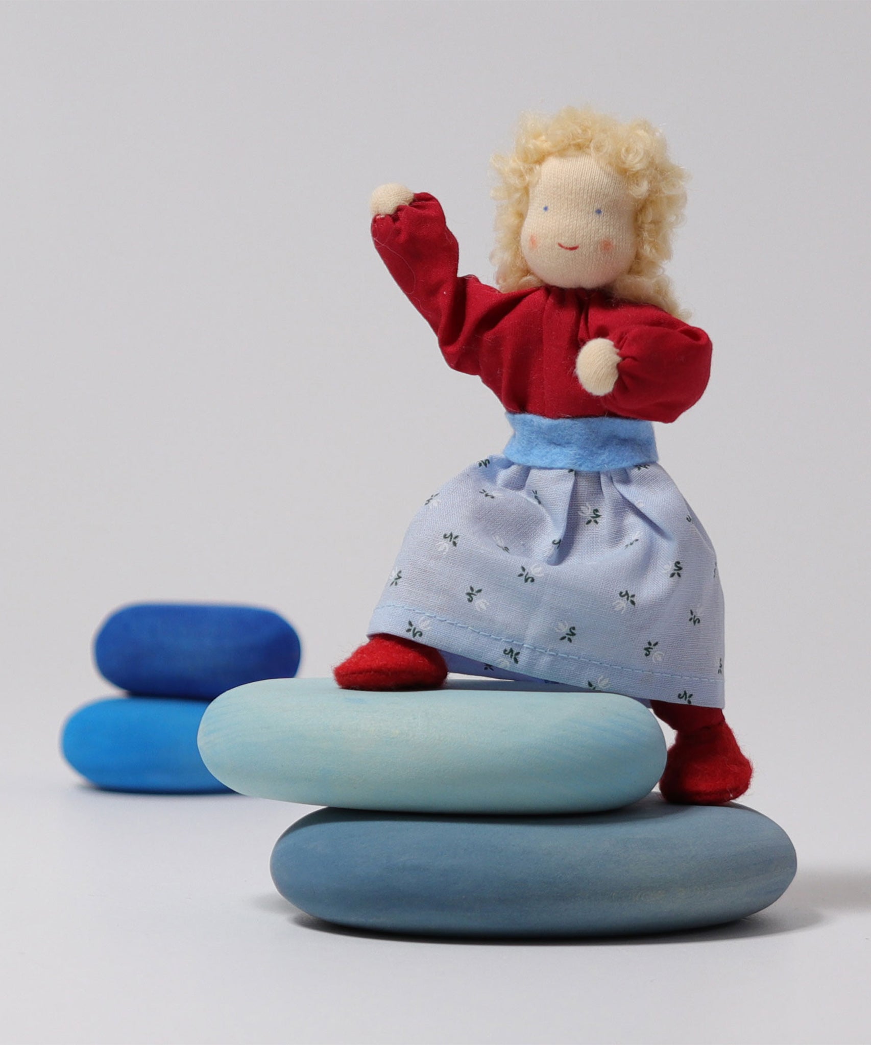 Grimm's Blonde Woman Doll is standing on the Blue Grimm's River Pebble pieces with its legs bent at the knees and its arms stretched up to show the flexibility of the doll