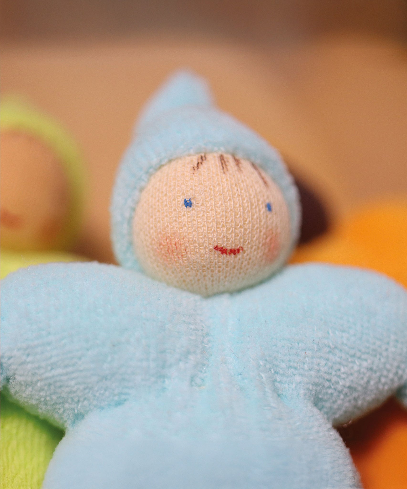 A closer look at the Grimm's Light Blue Pastel Dwarf face to show the doll's smiling face. The light blue dwarf doll has a red smile, light pink rosy cheeks, blue eyes and 4 brown painted strands of hair.