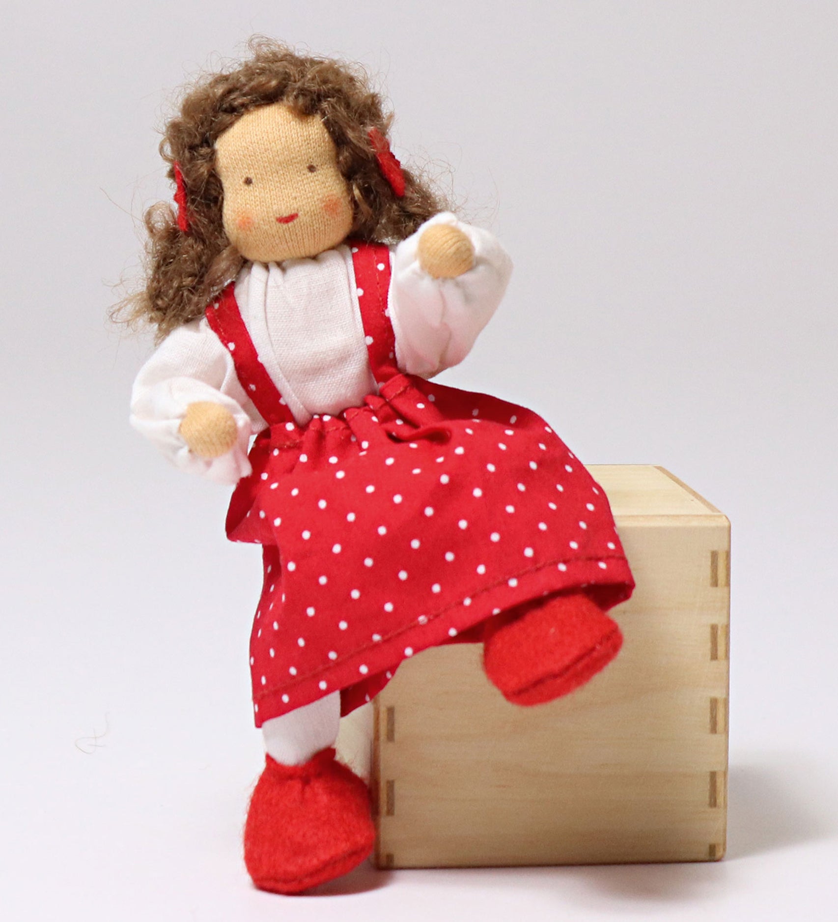 Grimm's Brown Haired Girl Doll - Lana is sat on a wooden block, showing the flexible arms and legs of the fabric doll