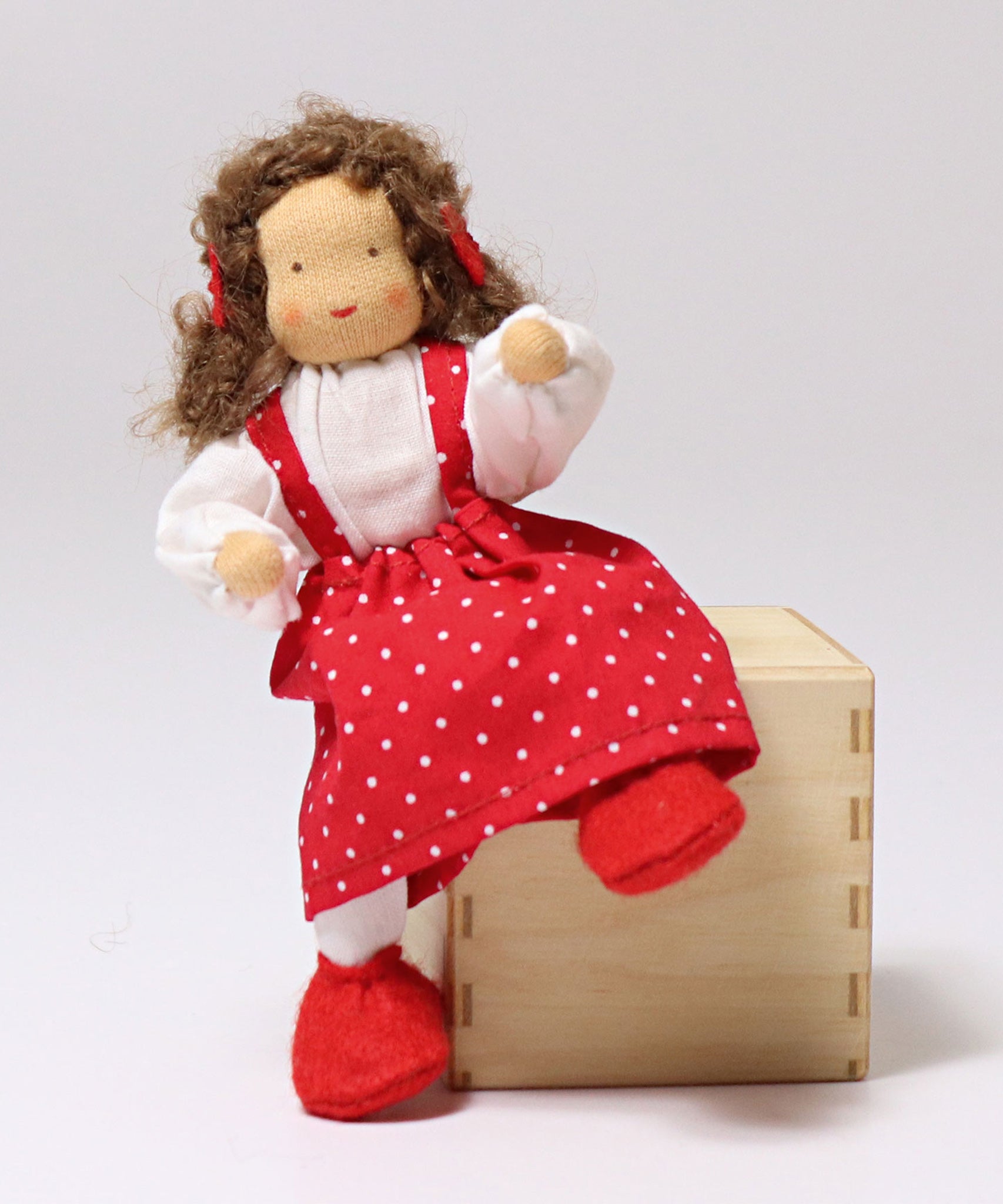 Grimm's Brown Haired Girl Doll - Lana is sat on a wooden block, showing the flexible arms and legs of the fabric doll