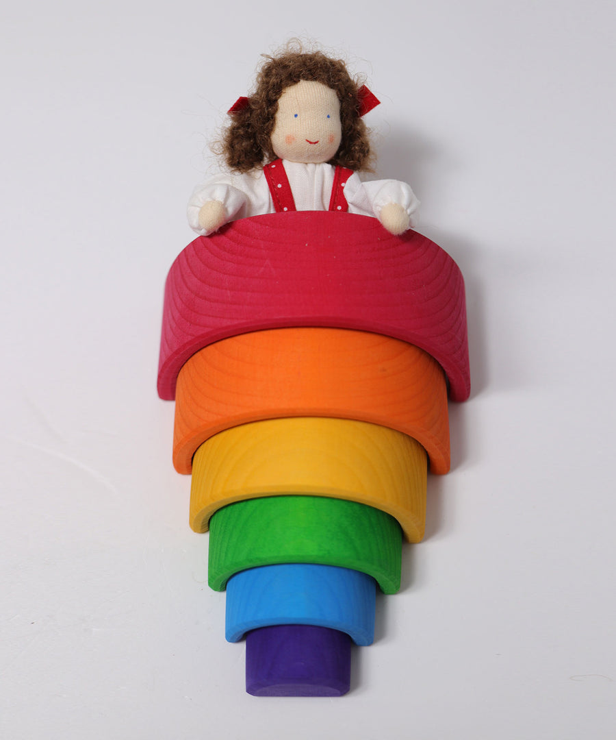 Grimm's Brown Haired Girl Doll - Lana is laid under a Grimm's Wooden rainbow with its hands on top of one of the rainbow arches