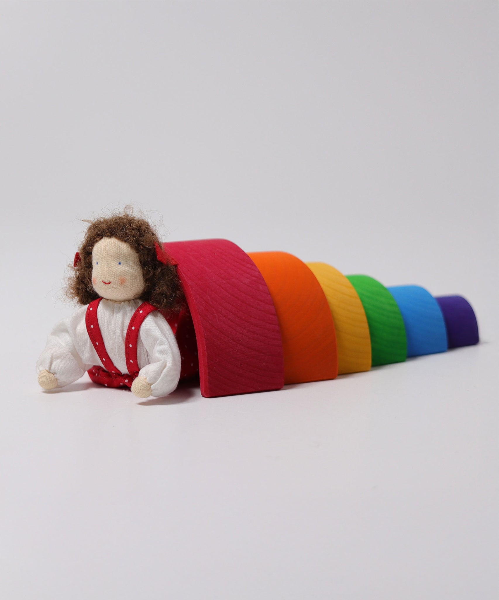 Grimm's Brown Haired Girl Doll - Lana is laid underneath a Grimm's Wooden Rainbow and is propped up on its arms and bend backwards slightly at the waist