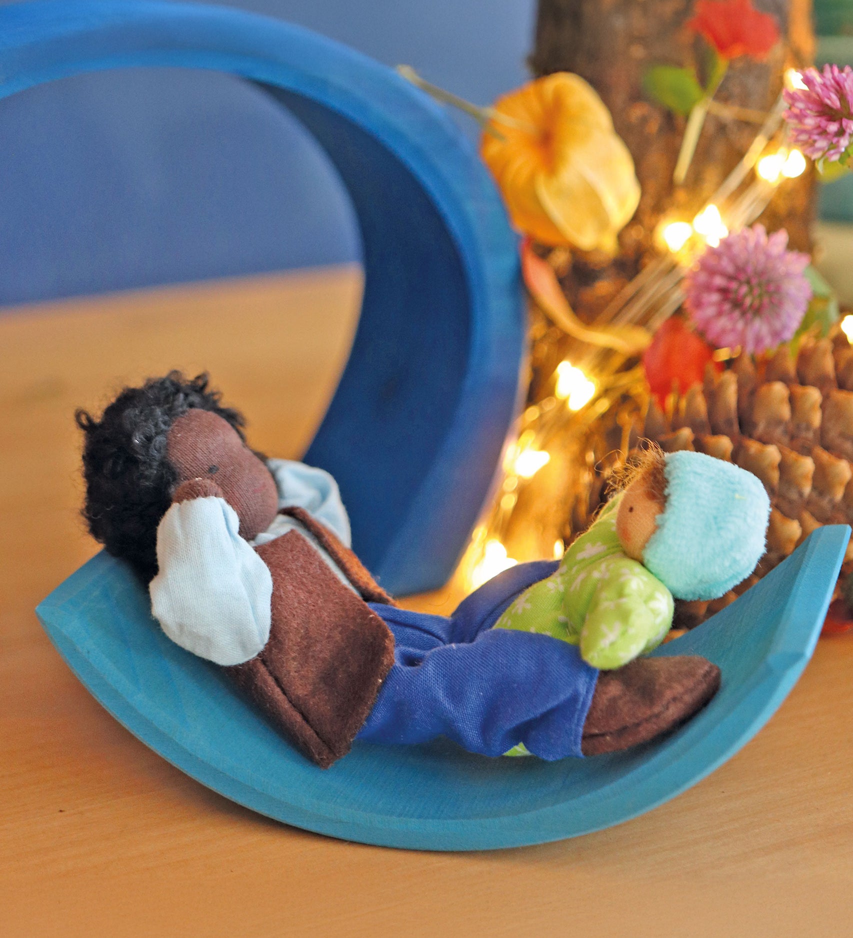 Mr Ebony and Baby Leo are playing on a light blue piece of a Grimms wooden toy. There are flowers and fairy lights in the background