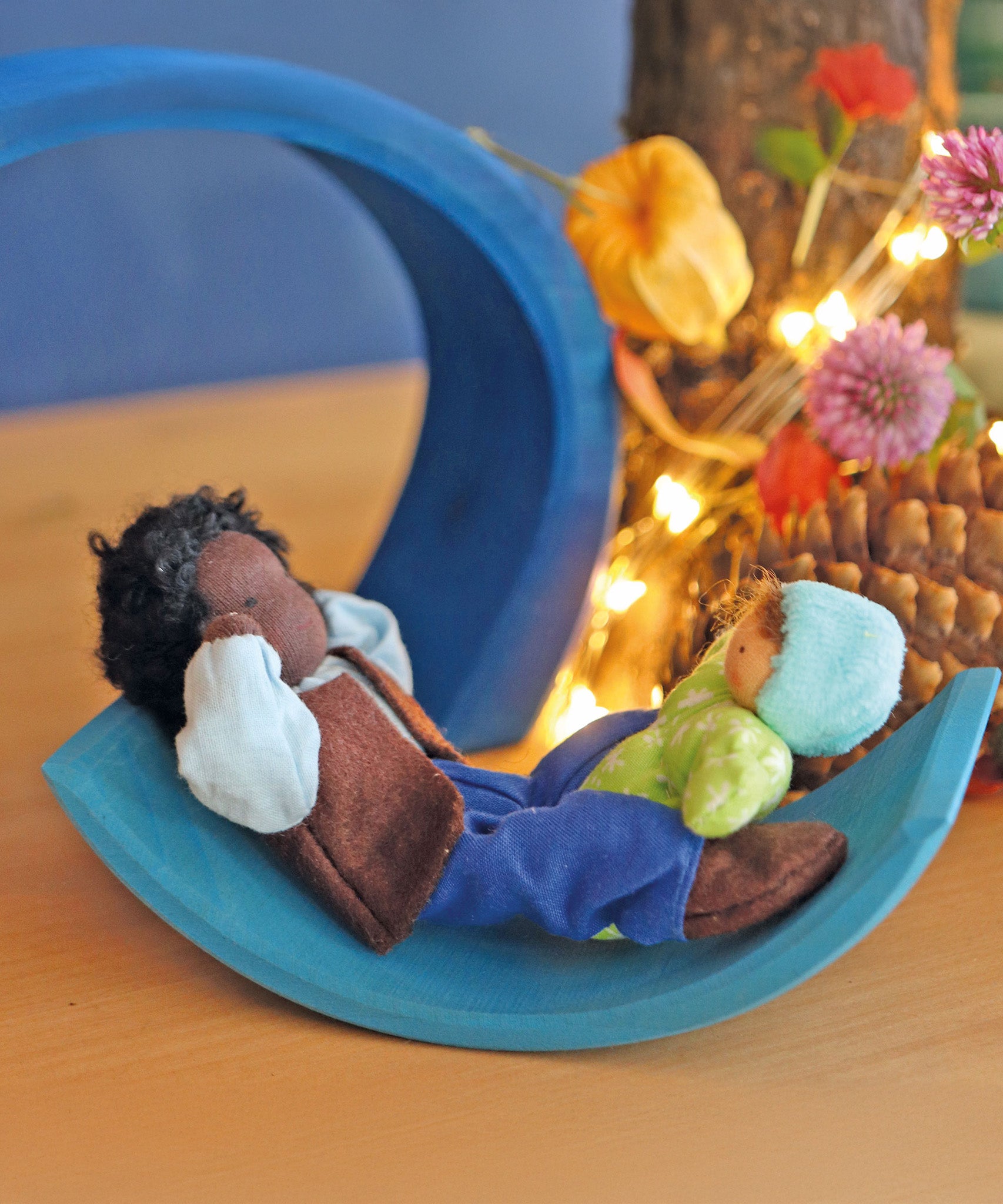 Mr Ebony and Baby Leo are playing on a light blue piece of a Grimms wooden toy. There are flowers and fairy lights in the background