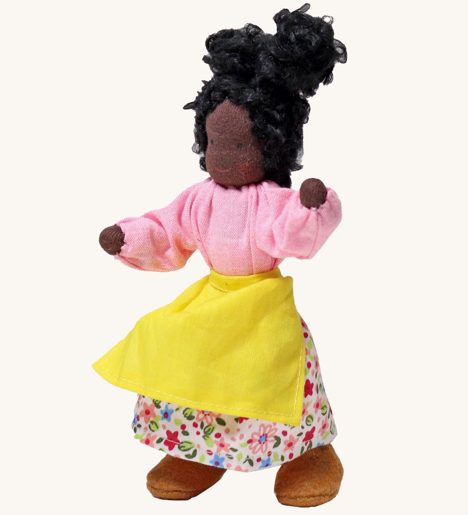 Grimm's Handmade Doll - Mrs Ebony, is a lovely female character doll with black skin, a smiling face, long curly black hair, a pink top and flowery skirt, a yellow apron and light brown fabric shoes. The image is on a cream background