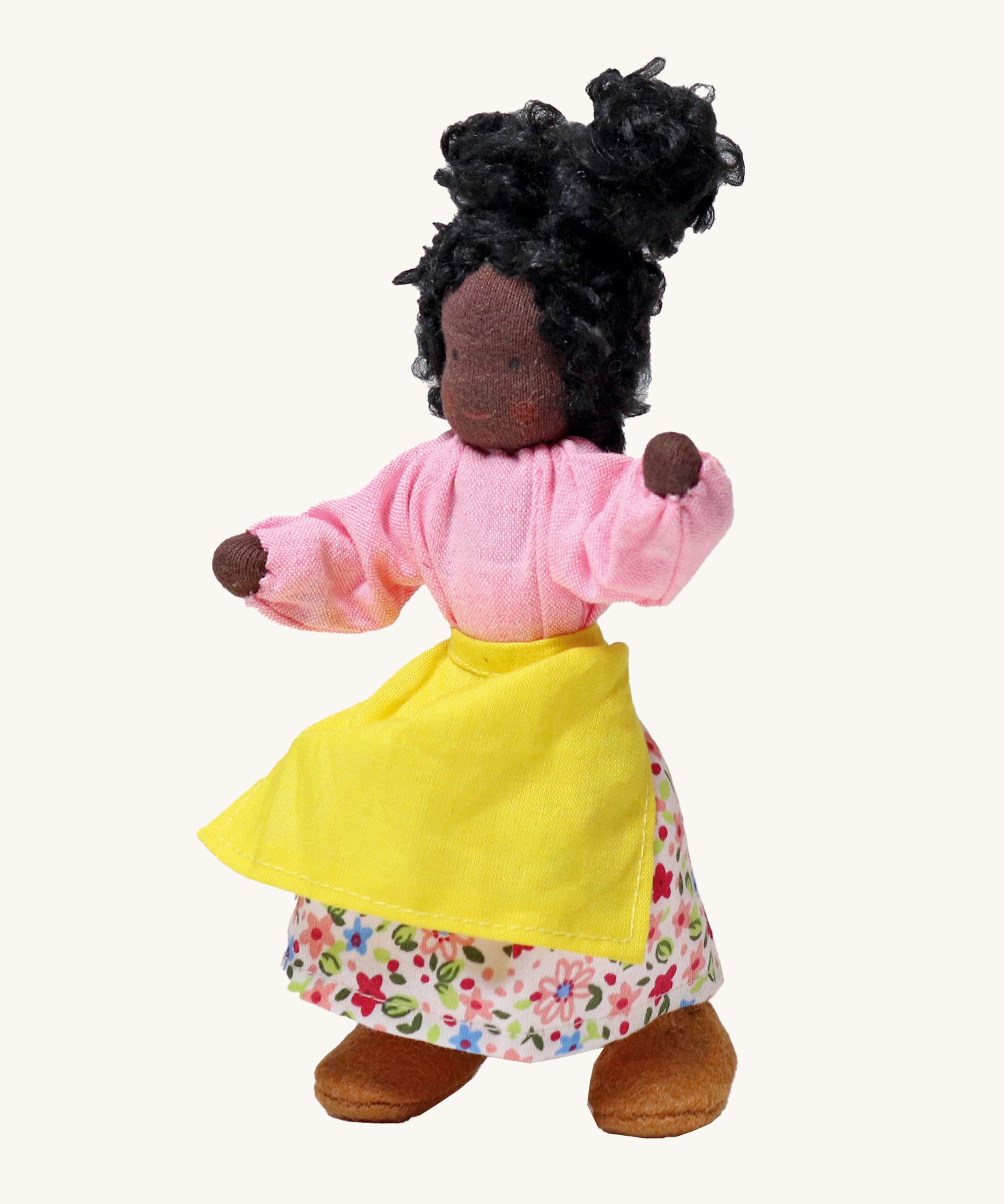 Grimm's Handmade Doll - Mrs Ebony, is a lovely female character doll with black skin, a smiling face, long curly black hair, a pink top and flowery skirt, a yellow apron and light brown fabric shoes. The image is on a cream background