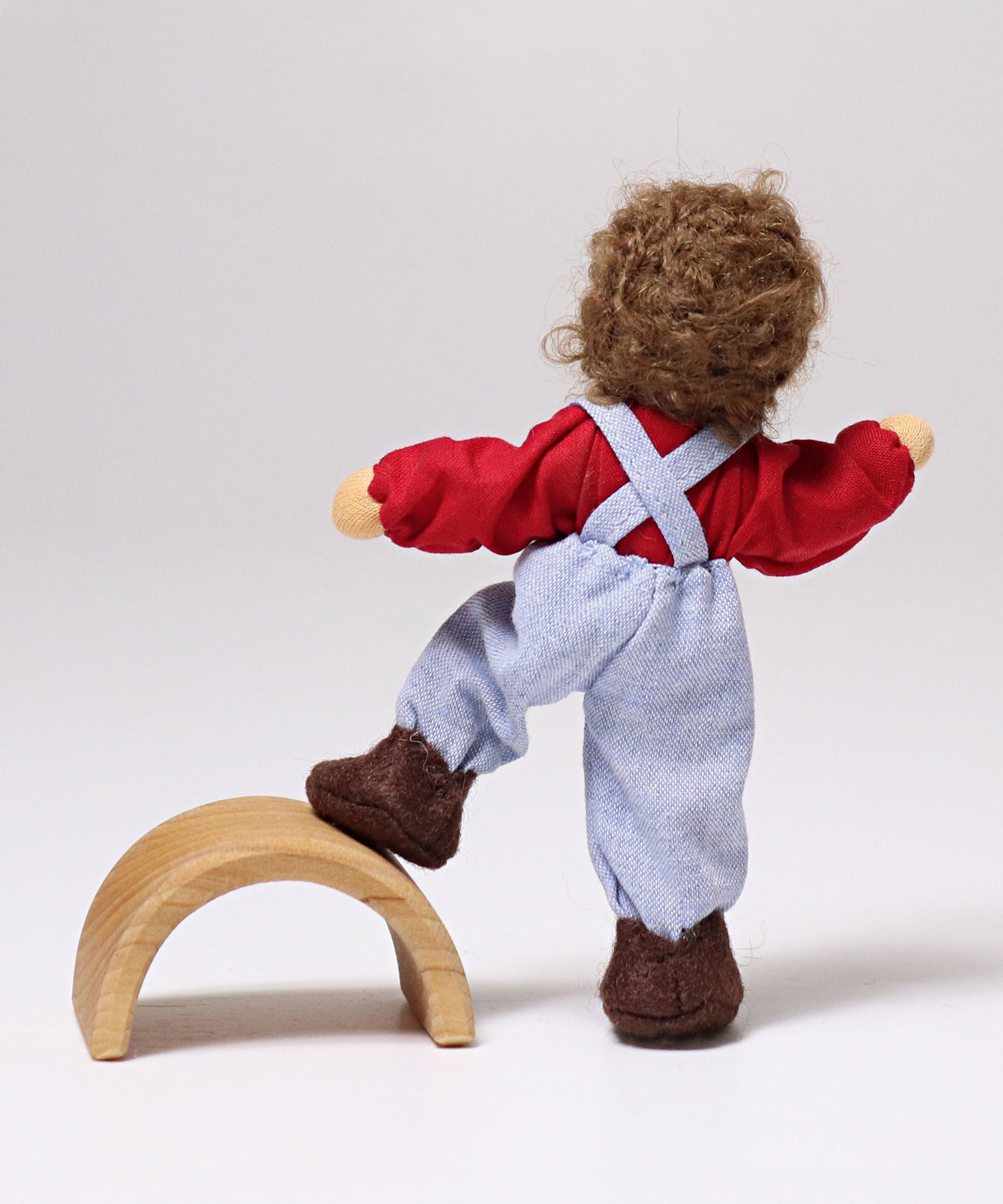 A behind shot of Grimm's Brown Haired Doll - Peter with its foot resting on a piece of Grimm's natural wooden rainbow. This image shows the flexibility of the dolls limbs