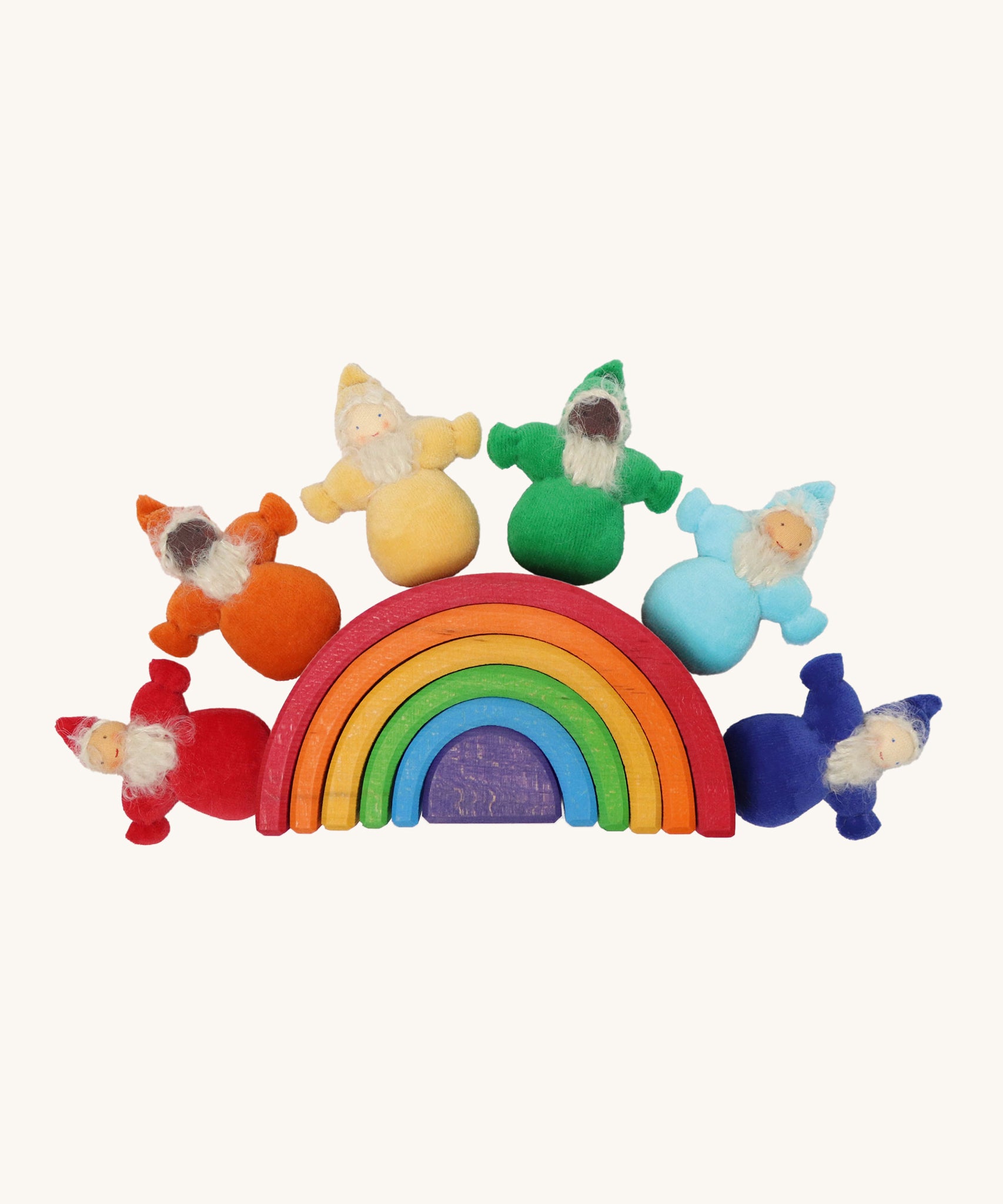 The Grimm's Rainbow Dwarfs toy dolls sat on top of a grimm's small wooden rainbow toy, on a cream background