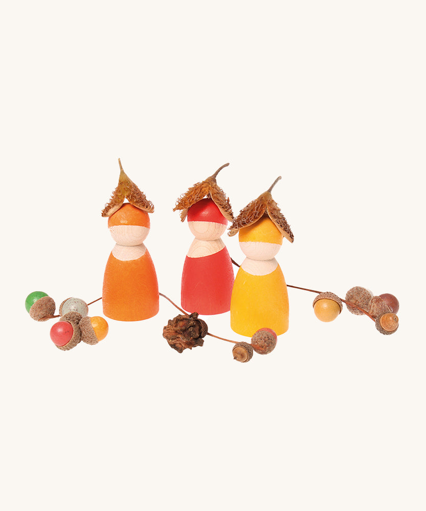 Three Grimm's Rainbow Friends wearing little horse chestnut shell hats with colourful acorns around them