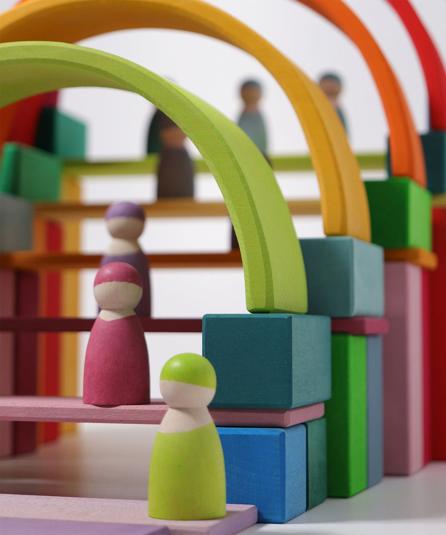 The Grimm's 12 Pastel Friends stood on a Grimm's building set up of colourful blocks and rainbow arches