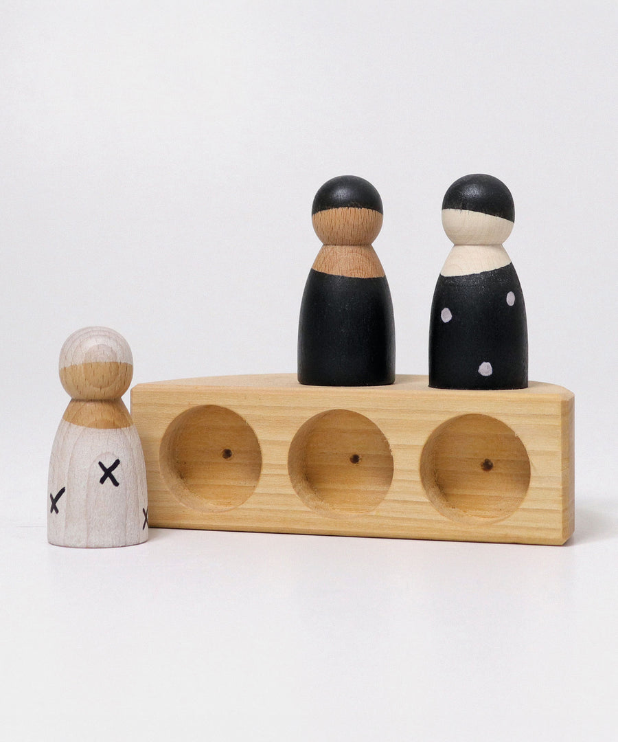 The Grimm's Natural Wooden boat on its side showing the holes for the wooden peg dolls to sit in. The Grimm's 3 in a Boat Monochrome peg dolls are stood on top and at the side of the boat