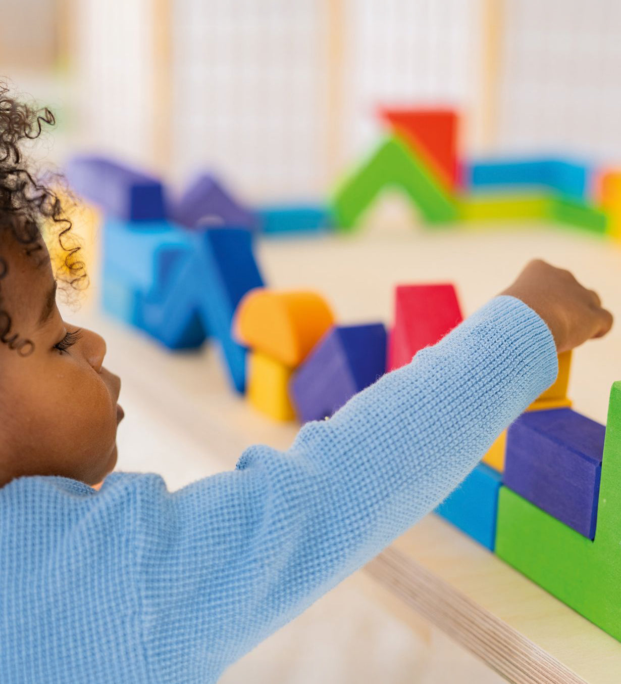 A child carefully puts a block on top of a wall they have created using the Grimm's Basic Building Set