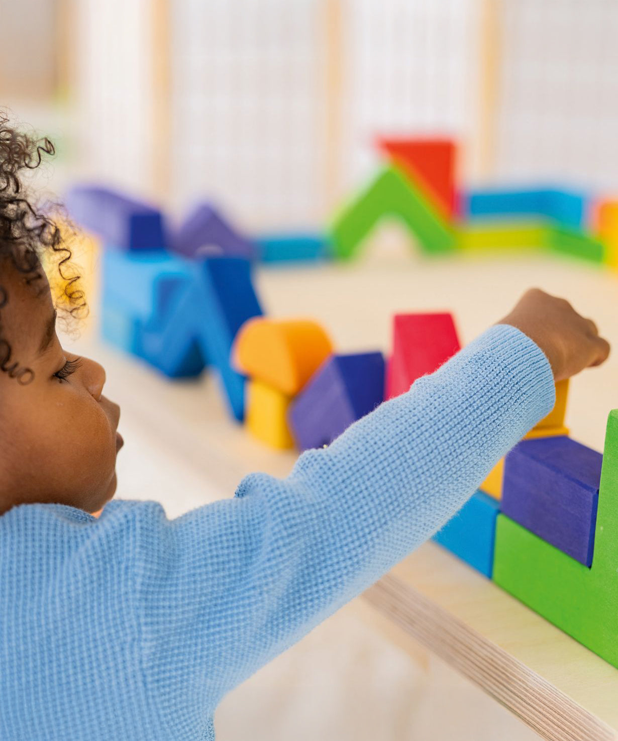 A child carefully puts a block on top of a wall they have created using the Grimm's Basic Building Set