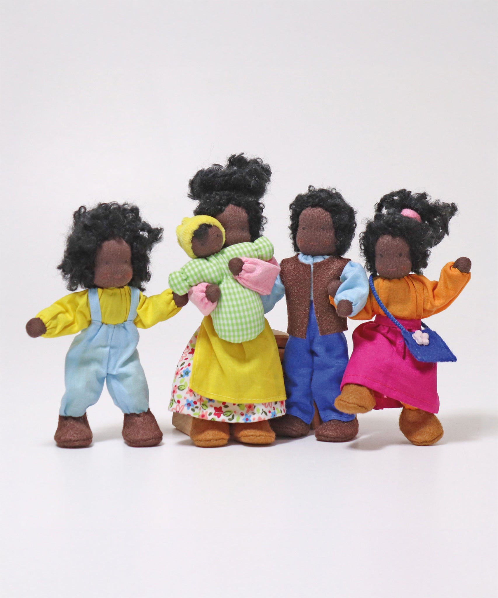 The Grimm's Handmade Waldorf Doll Family includes Mr Ebony, Mrs Ebony, Lisa, Max and Baby Sam. The dolls are all stood together with Mrs Ebony holding baby Max