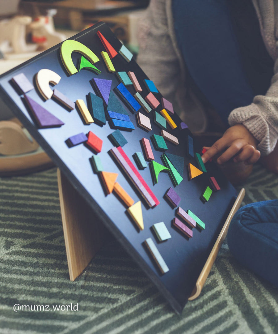 A child playing with the Grimm's Magnetic Blackboard, and has created a pattern using the Grimms magnetic puzzle pieces