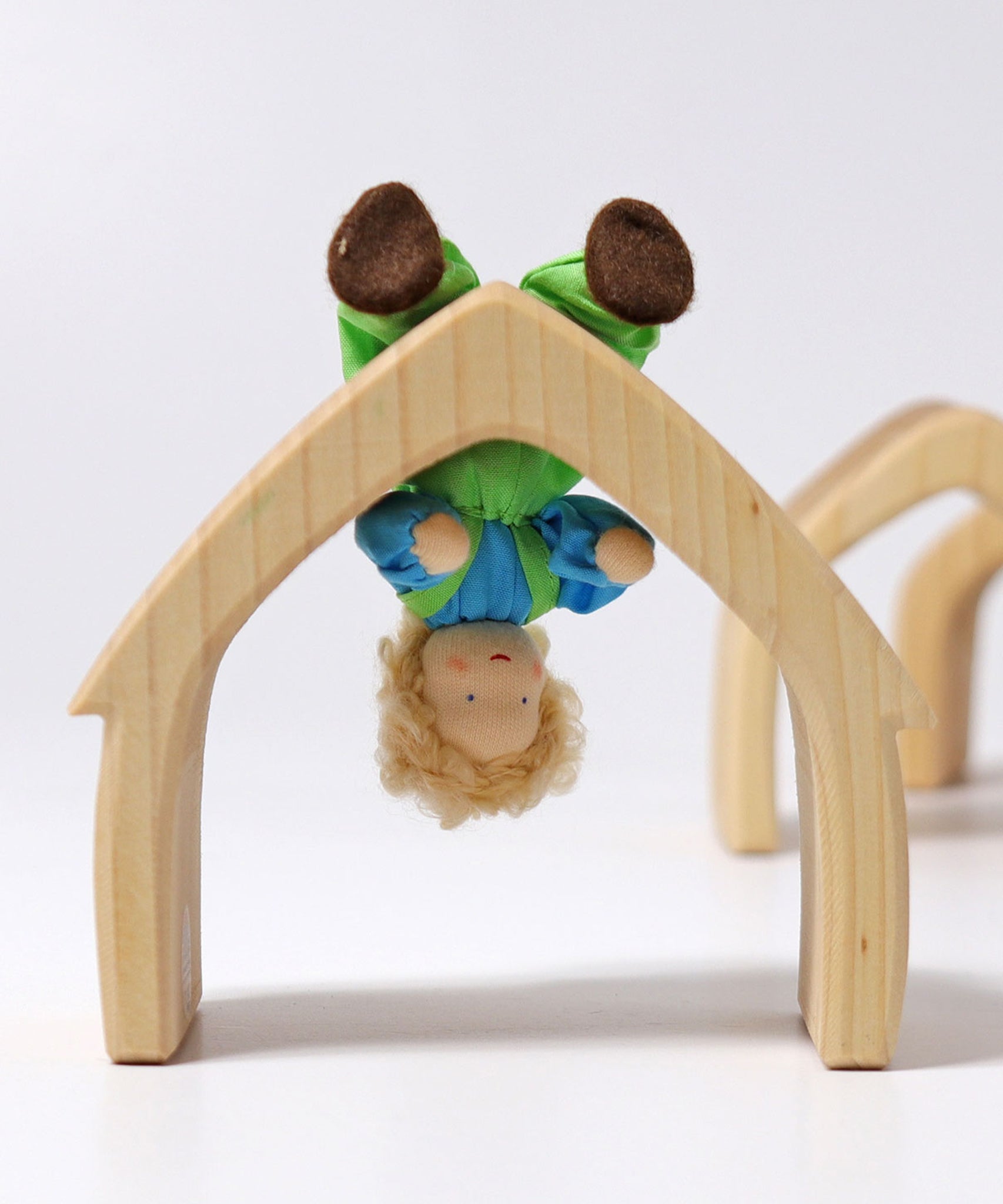 Grimm's Blond Boy Doll - Linde is bent at the waist and is hanging upside down on a Grimm's natural arch to show the flexibility of the doll