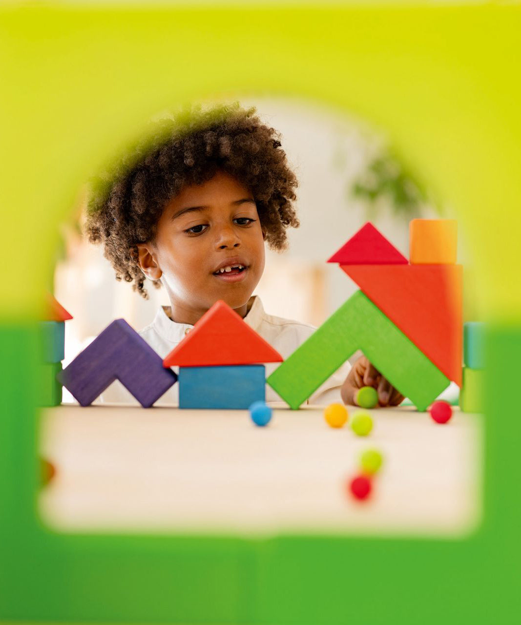 Two building blocks have been put together to create a window effect, and looking through you can see a child playing with small colourful marbles and the Grimm's Basic Building Set