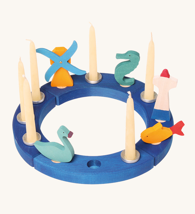 Grimm's 12-Hole Blue Wooden Ring has candles and small Grimm's decorative figures in each hole, and is on a cream background