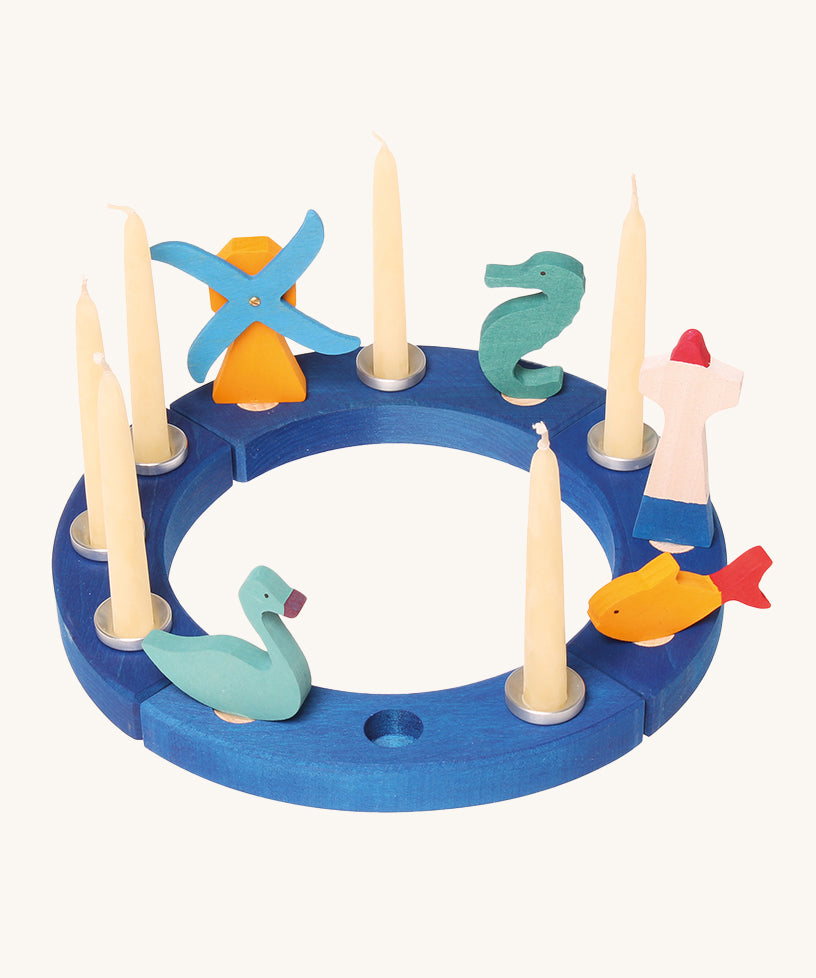 Grimm's 12-Hole Blue Wooden Ring has candles and small Grimm's decorative figures in each hole, and is on a cream background