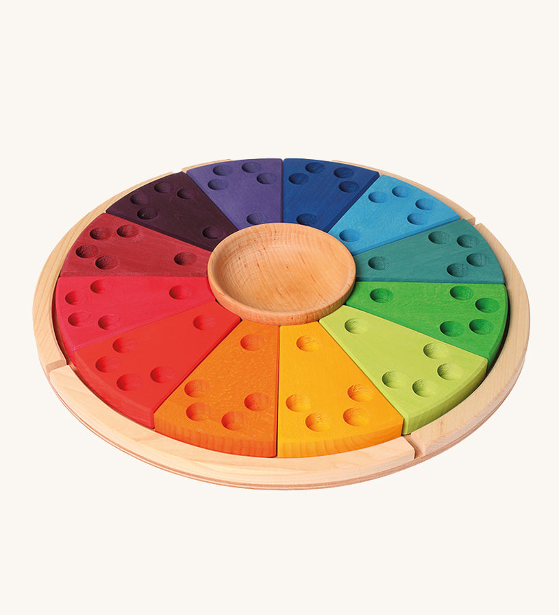 Grimm's Annual Celebration Ring, is made from 12 colourful section with small holes inside ready to lot in candles and colourful numbers, letters and characters into the holes. There is also a small wooden bowl in the middle and it is on a light wooden base. The image is on a cream background