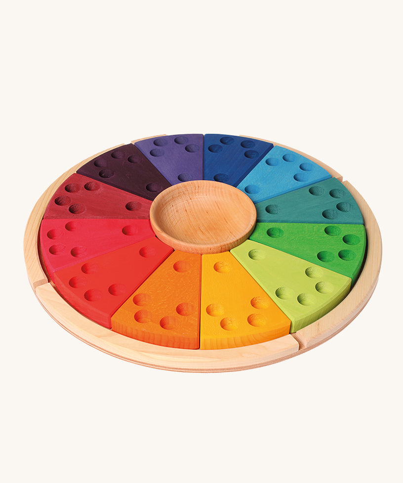 Grimm's Annual Celebration Ring, is made from 12 colourful section with small holes inside ready to lot in candles and colourful numbers, letters and characters into the holes. There is also a small wooden bowl in the middle and it is on a light wooden base. The image is on a cream background