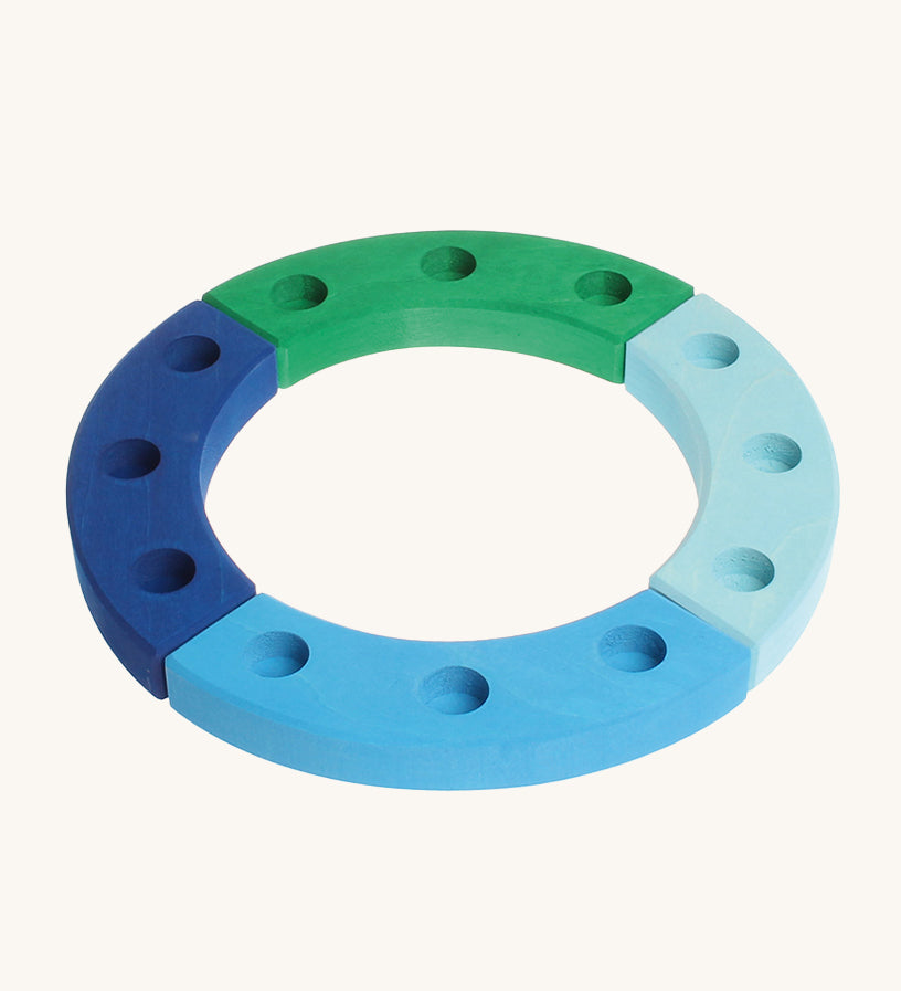 Grimm's 12-Hole Blue-Green Wooden Celebration Ring is made from 4 separate sections of wood with 3 holes to add Grimm's decorative figures and candles inside. The image is on a cream background. 