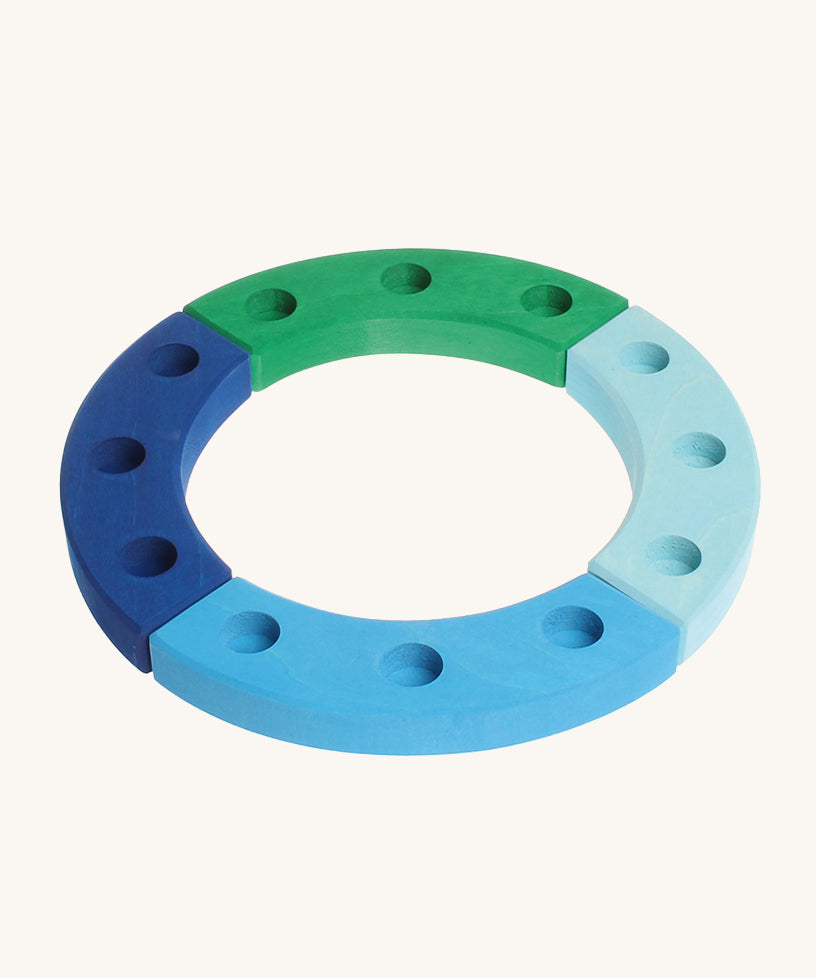 Grimm's 12-Hole Blue-Green Wooden Celebration Ring is made from 4 separate sections of wood with 3 holes to add Grimm's decorative figures and candles inside. The image is on a cream background. 