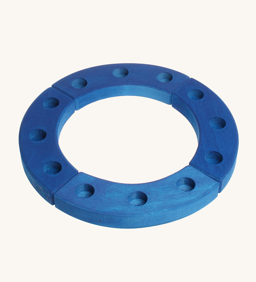 Grimm's 12-Hole Blue Wooden Ring is made from 4 sections of wood, with each section having 3 hold to put a decorative figure or a candle inside. The image is on a cream background