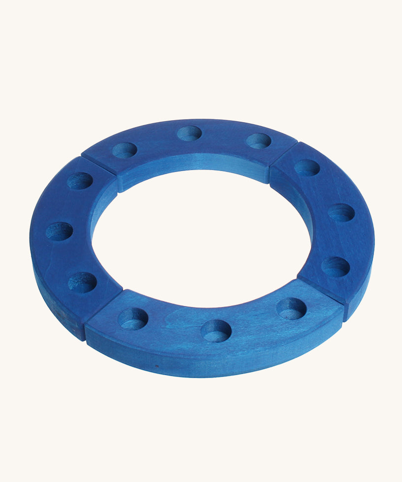 Grimm's 12-Hole Blue Wooden Ring is made from 4 sections of wood, with each section having 3 hold to put a decorative figure or a candle inside. The image is on a cream background