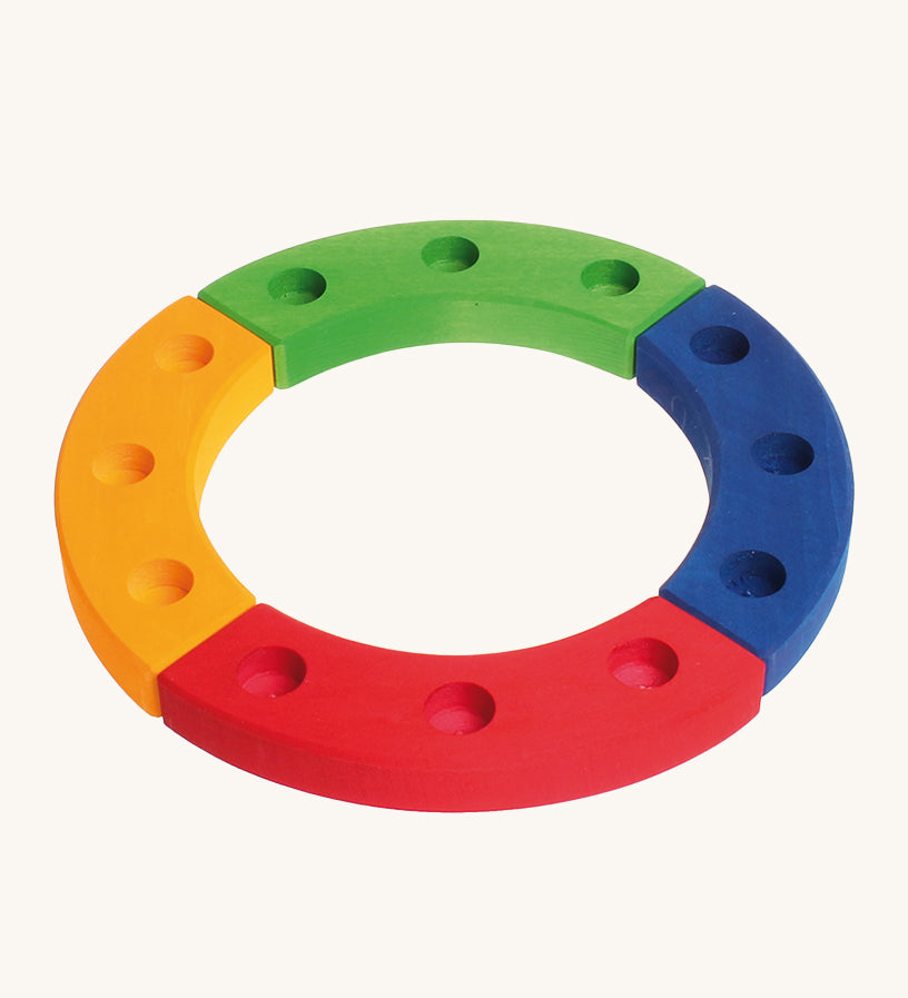 Grimm's 12-Hole Coloured Wooden Ring is made up from 4 sections of wood, yellow, red, green and blue, with 3 holes to add Grimm's decorative figures and candles inside. The image is on a cream background