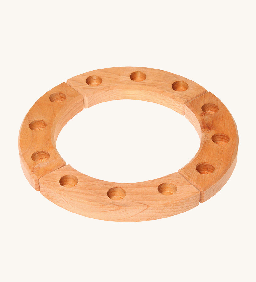 Grimm's 12-Hole Natural Wooden Celebration Ring is made from 4 sections of natural wood with 3 holes in each section, ready for Grimm's decorative figures and candles to be placed inside. The image is on a cream background.