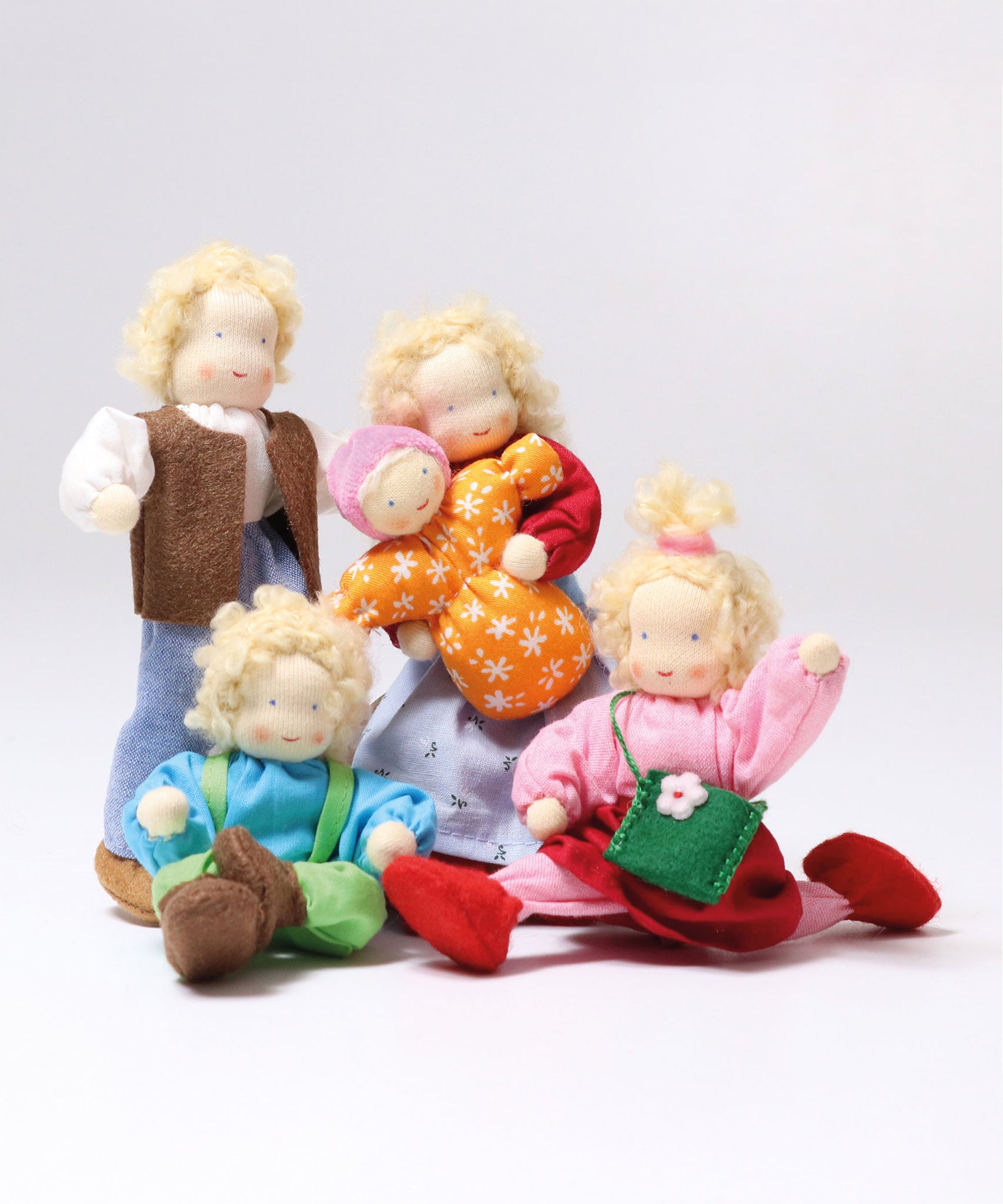 The Grimm's Waldorf Dolls Family are all together, and on a grey background. The family are Grimm's Blond Haired Woman Doll, Grimm's Blond Haired Girl Doll, Baby Mia,  Blonde Haired Male Doll and Blonde Haired Boy Doll - Linde.