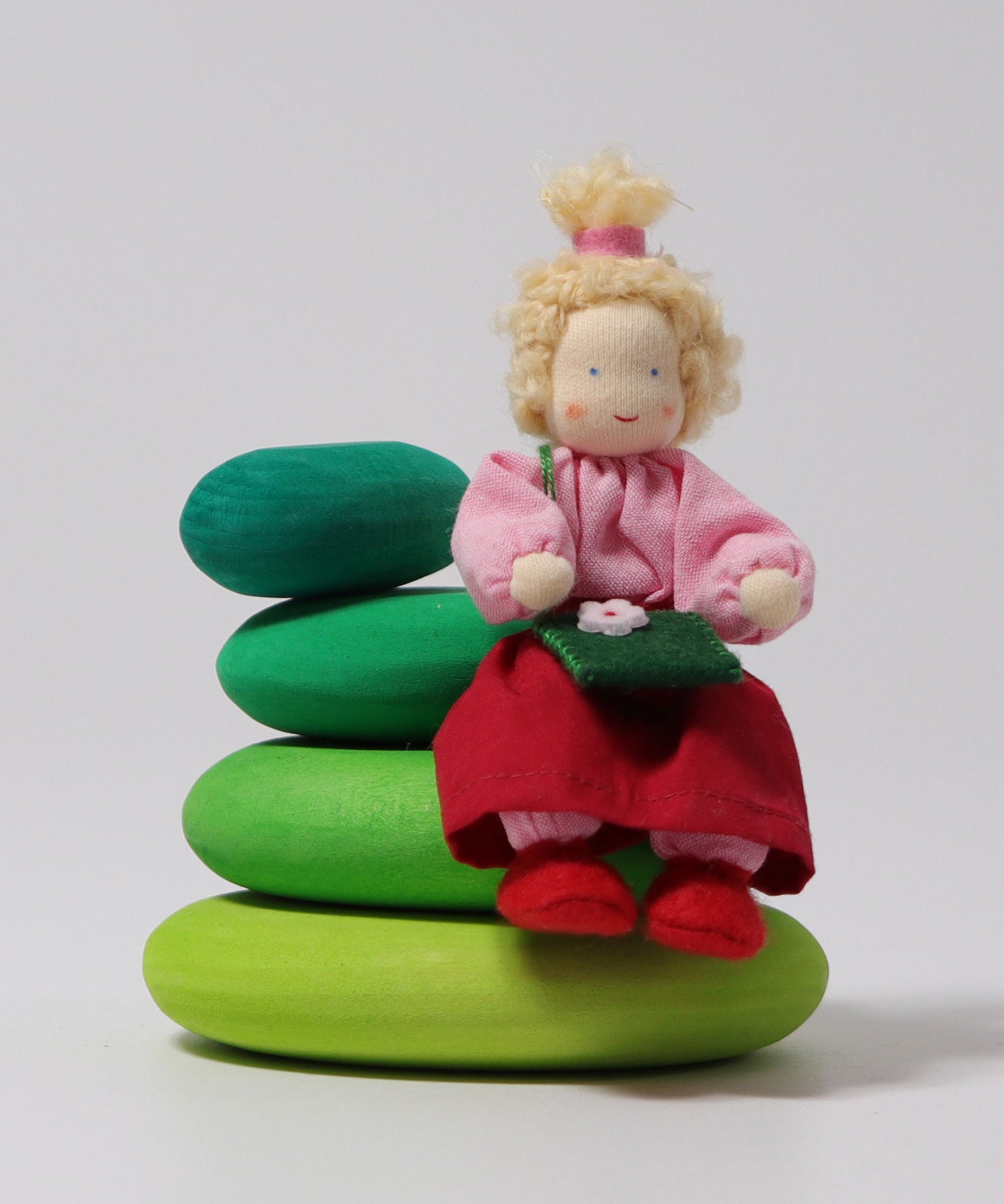 The Grimm's Blonde Girl Doll, sitting down on the Grimm's Moss Pebbles Building Set, on a grey background