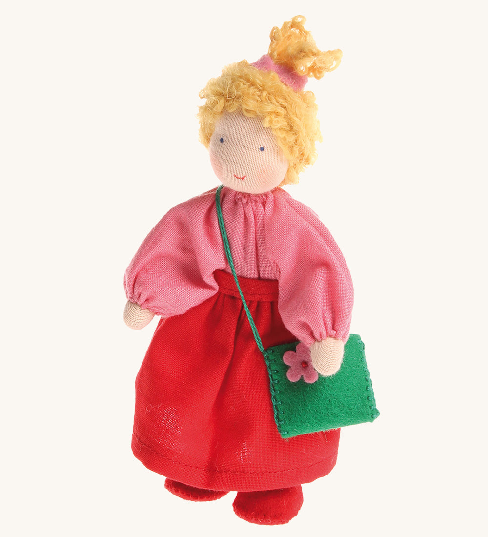 Grimm's Waldorf Blonde Girl Doll wearing a pink top, a red skirt and carrying a green felt bag with a pink flower, on a cream background